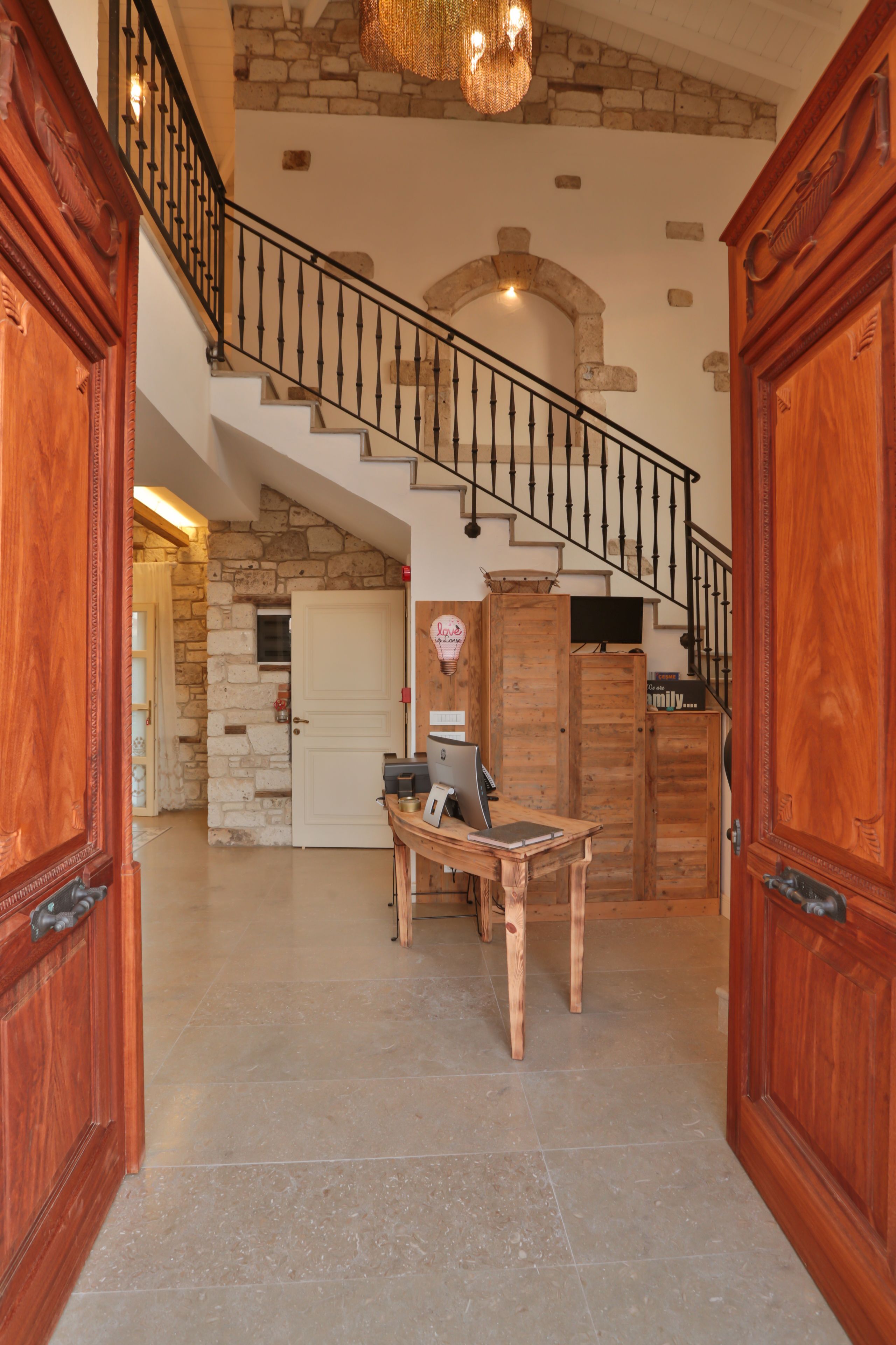 A spacious foyer with a stone staircase, wooden doors, and a desk with a computer.