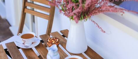Una mesa de madera con dos tazas de café, un cuenco pequeño de nueces y un florero blanco con flores rosadas.