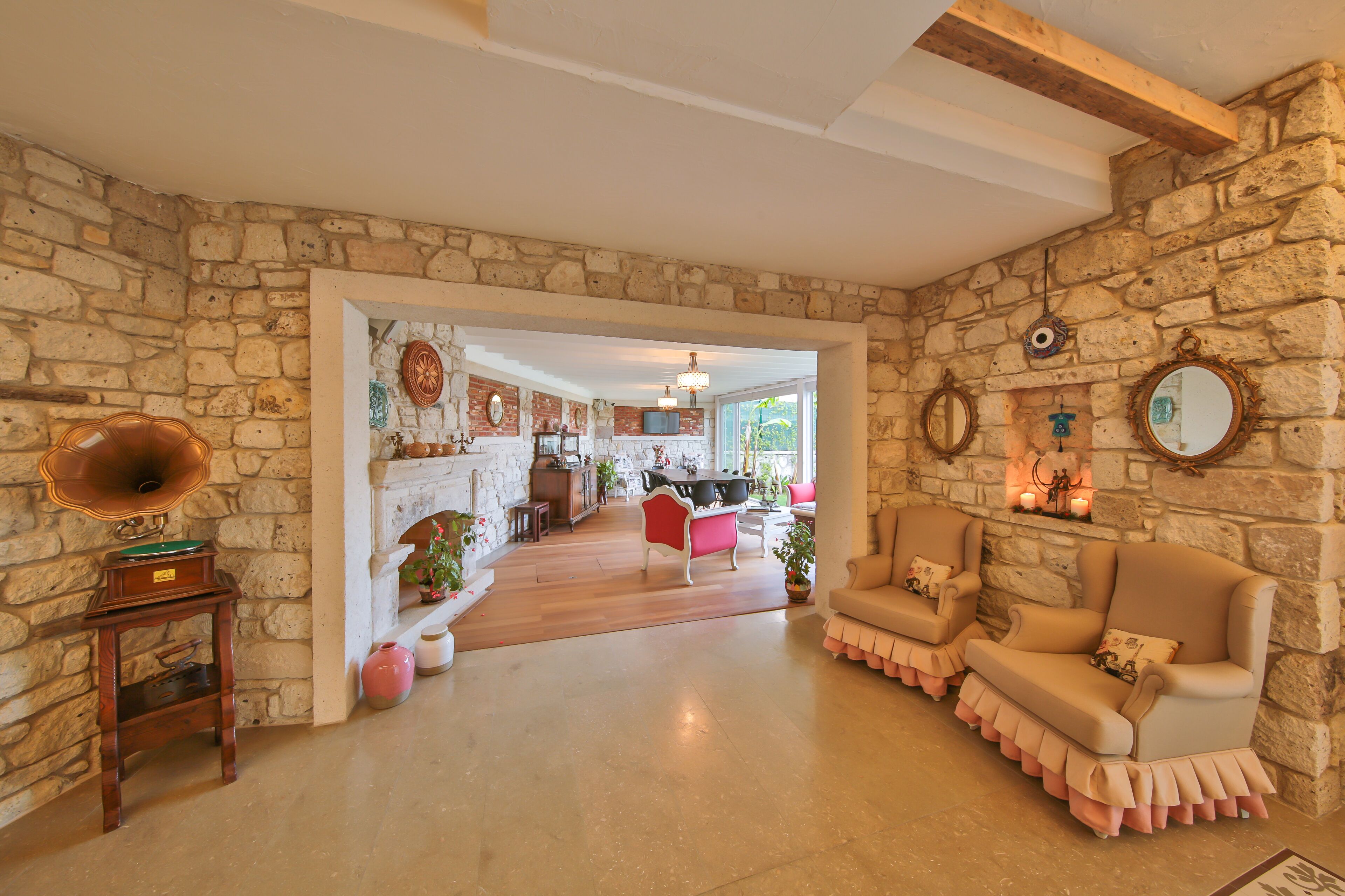 A stone-walled room with a fireplace, a dining area, and a seating area with two armchairs and a sofa.