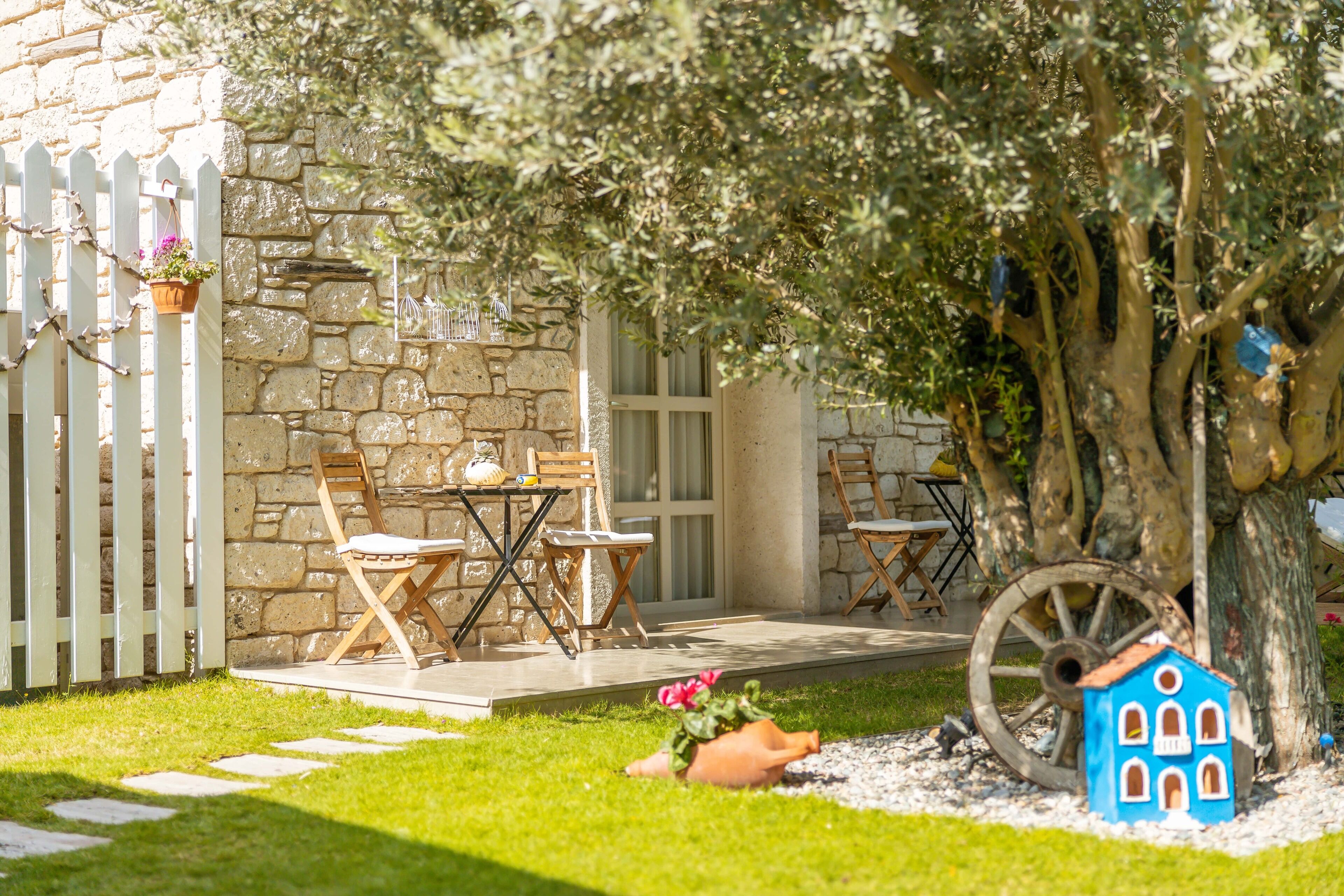 A stone building with a white picket fence, outdoor seating, and a decorative tree house.