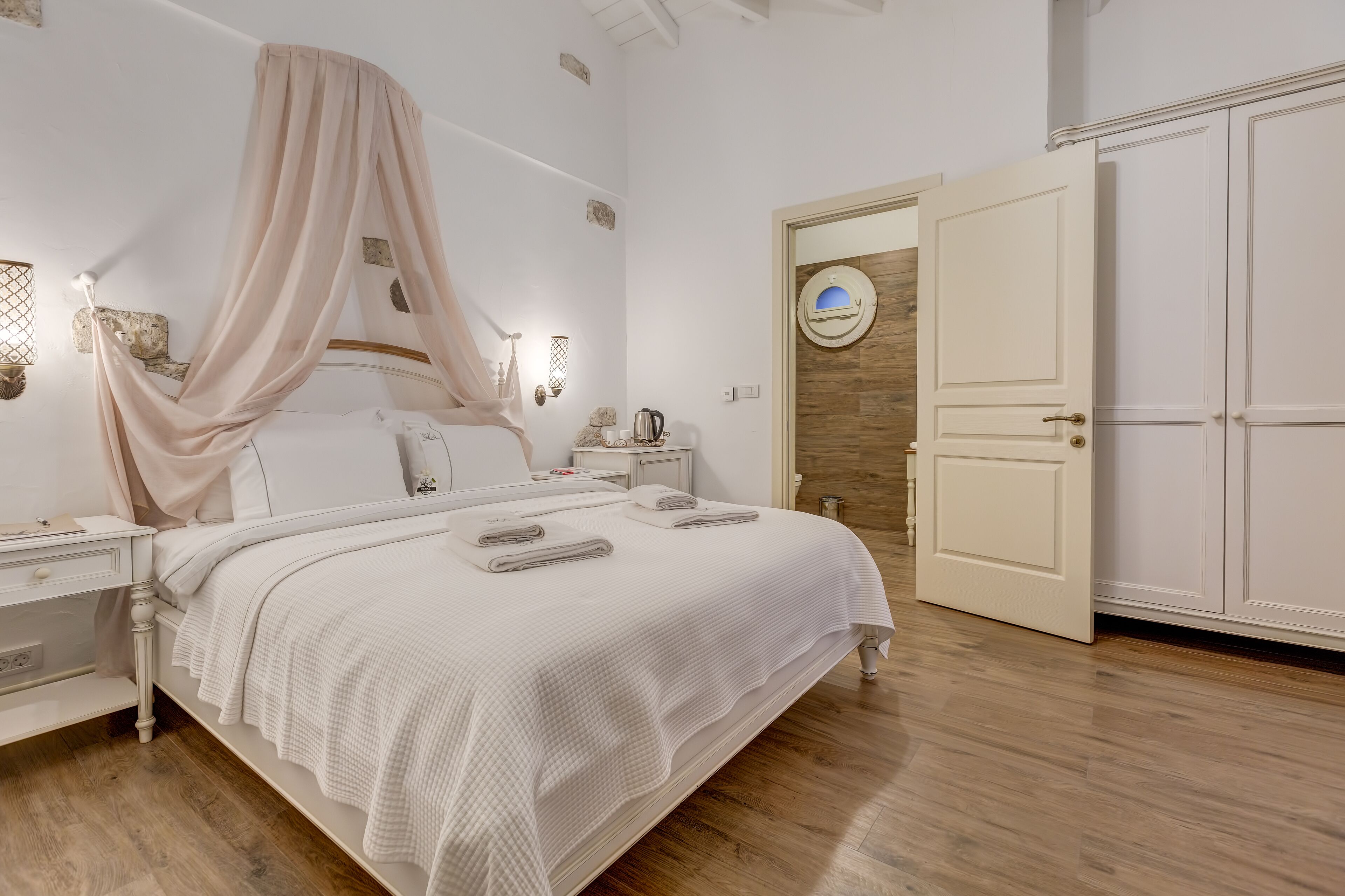 A neatly arranged bedroom with a canopy bed, bedside tables, a wardrobe, and a wooden floor.