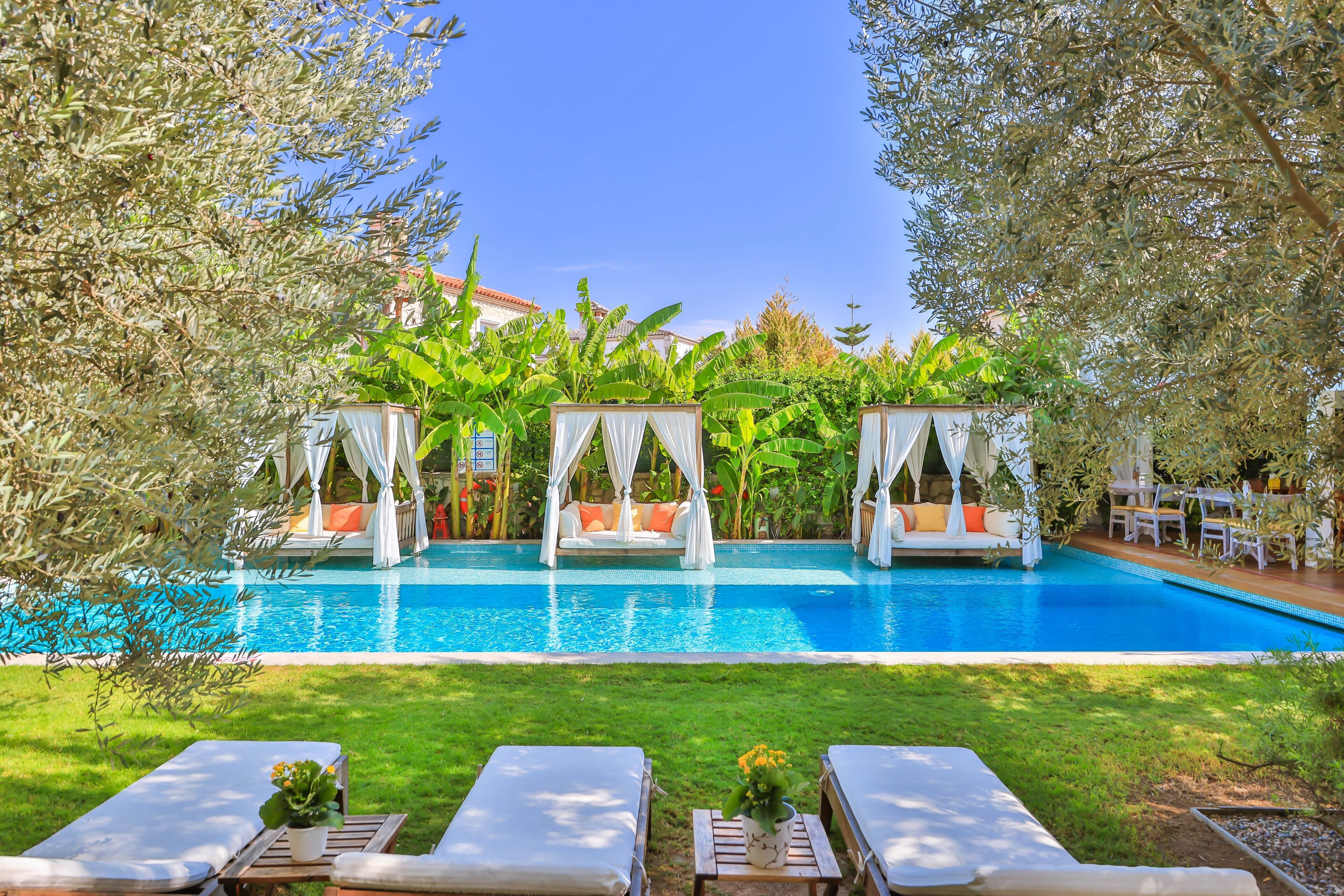 Un espace piscine comprenant trois cabanas, des chaises longues et une piscine à l’eau d’un bleu cristallin.