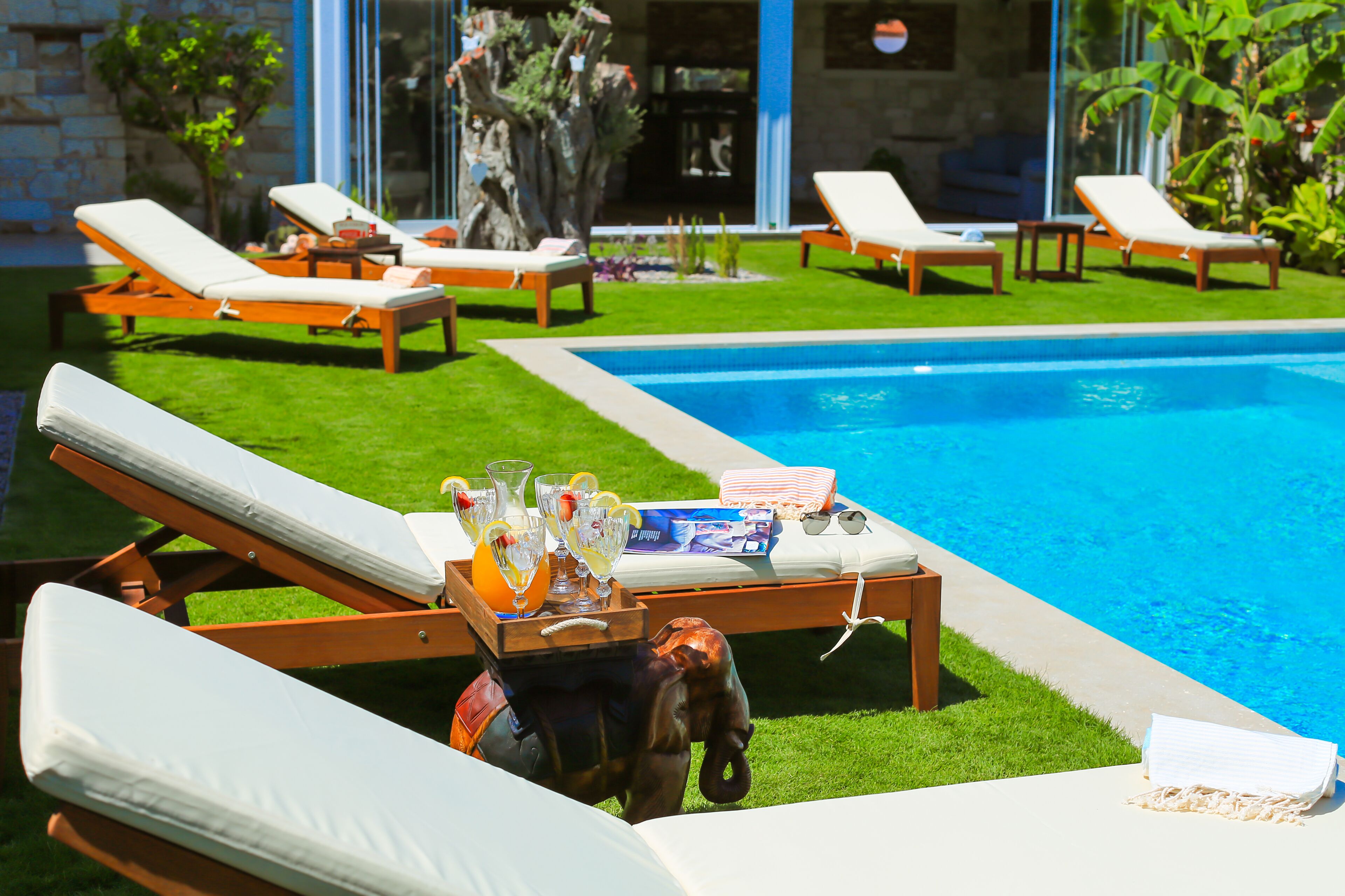 A poolside area with lounge chairs, a wooden table with drinks, and a small elephant statue.