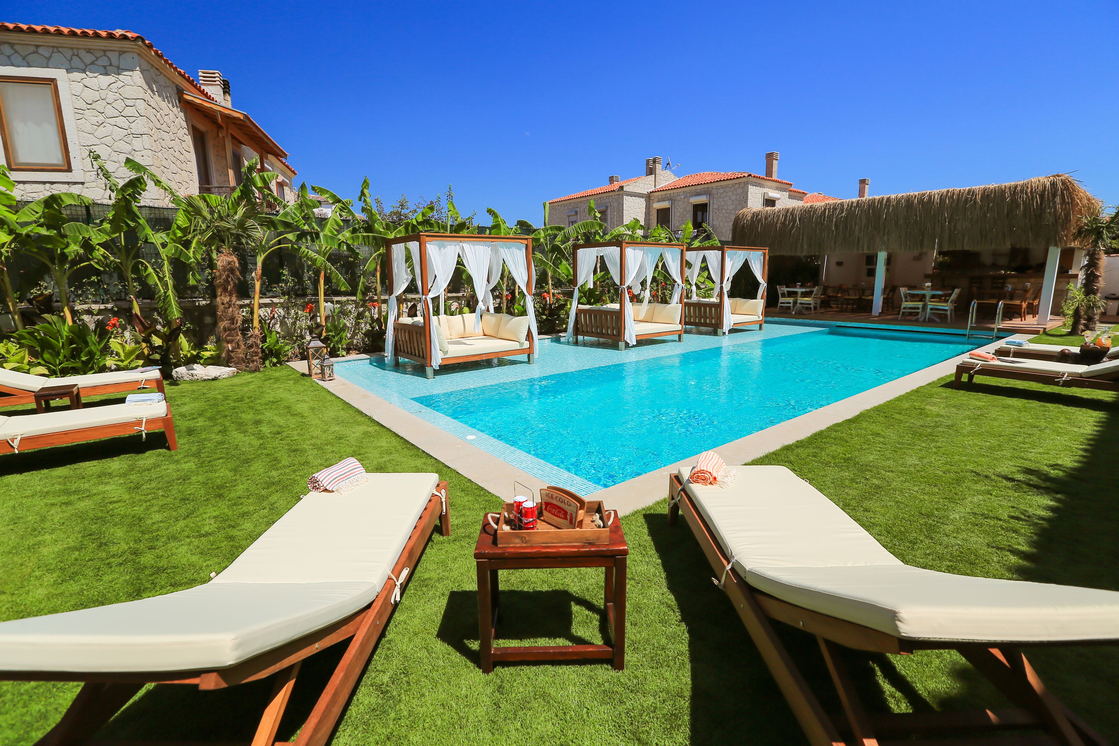 A pool area with lounge chairs, a small table with a drink, and a thatched-roof structure.