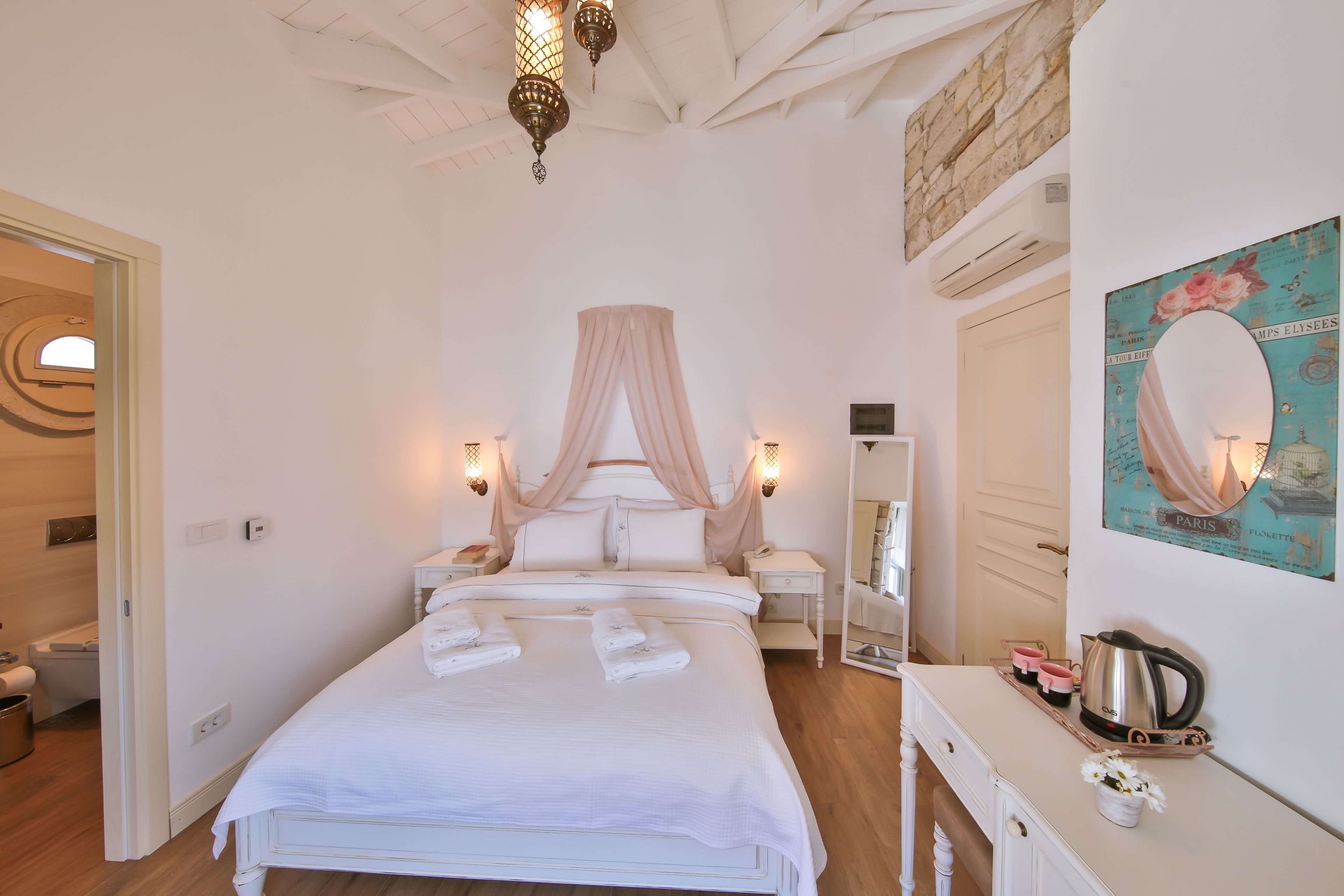 Ein ordentlich eingerichtetes Schlafzimmer mit einem Himmelbett, Nachttischlampen, einem Spiegel und einem kleinen Tisch mit Wasserkocher und Tassen.