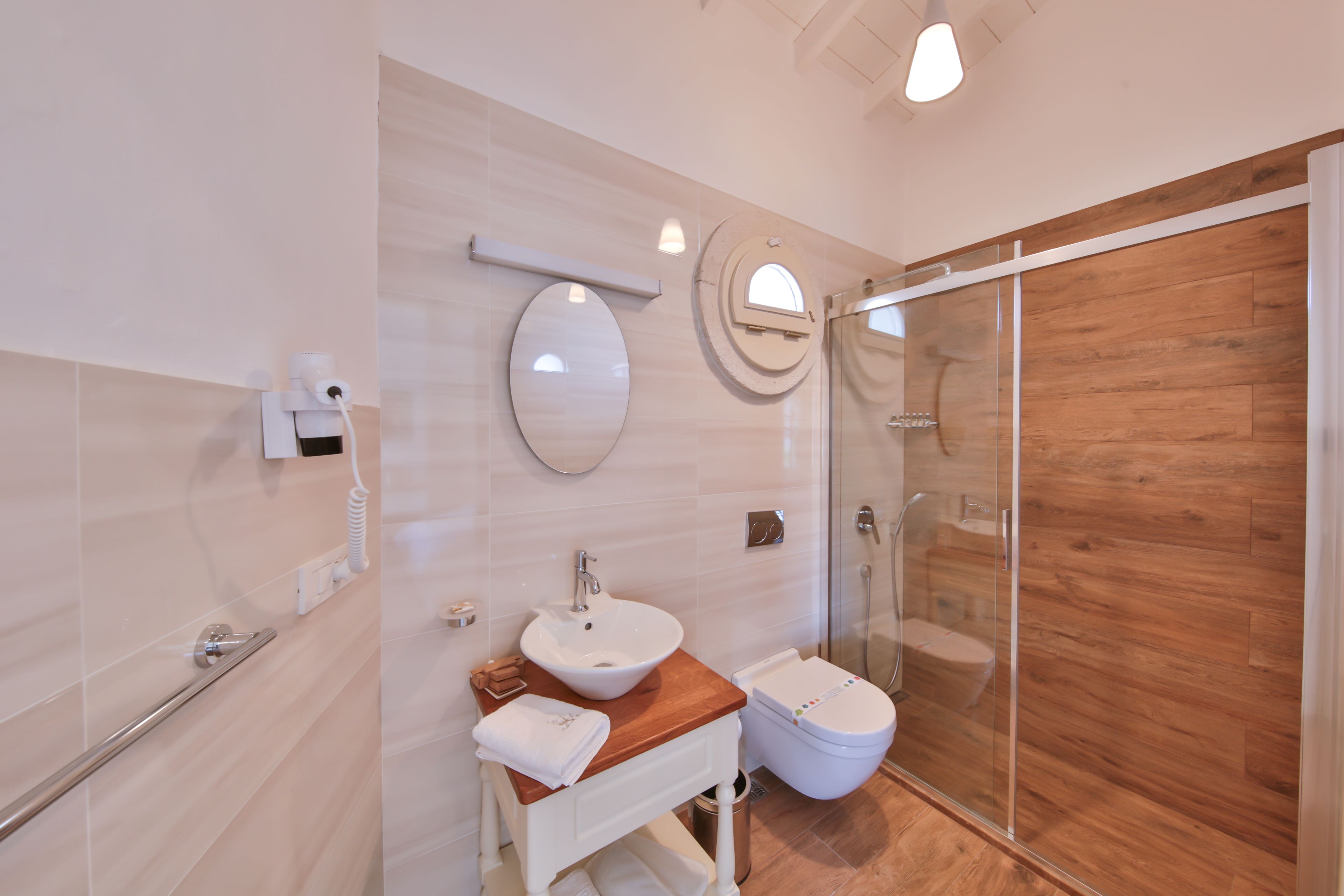 A modern bathroom with a wooden floor, a white sink, a glass shower enclosure, and a toilet.