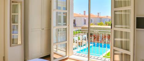 A hotel room with a bed, a tray with breakfast, a view of a pool, and a balcony with curtains.