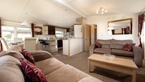 A spacious living area with a sofa, a coffee table, and a kitchen in the background. - Sandy Meadows Lodge Park (Burnham-on-Sea)