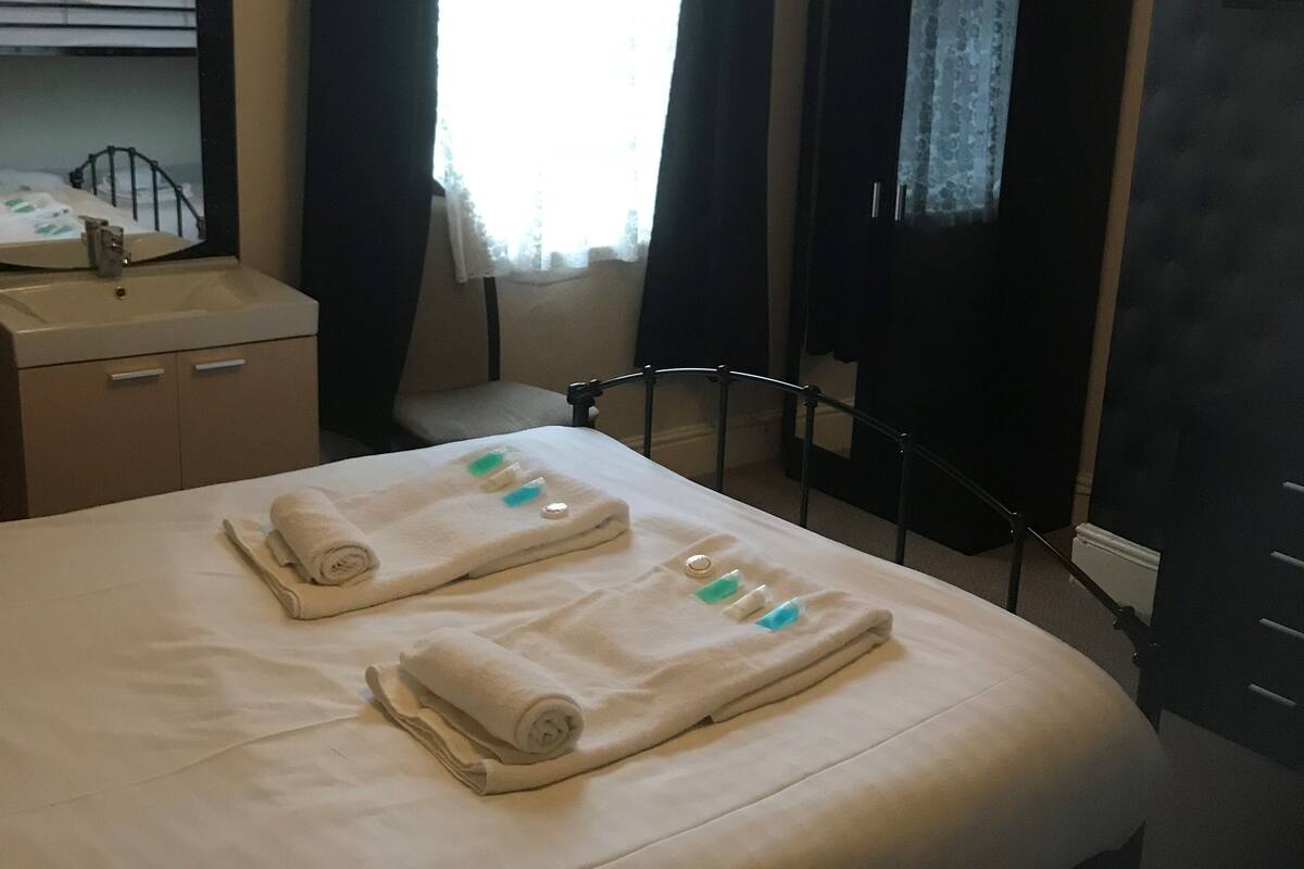 A hotel room with a bed, a bedside table, a mirror, a window with curtains, and a wardrobe.