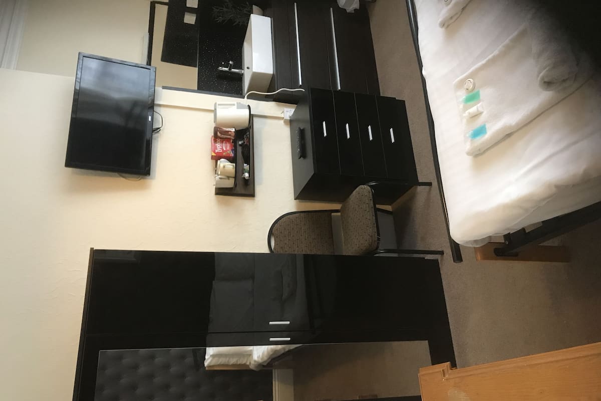 A room with a bed, a desk, a chair, a TV, and a small kitchenette area.
