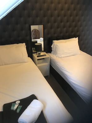 Hotelkamer met twee eenpersoonsbedden, een nachtkastje met lamp, een spiegel en een klein tafeltje met toiletartikelen.