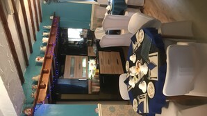 A dining area with a high table set for four, surrounded by chairs. There is a wooden bench along the wall with decorative lights. - South Dene Hotel (Bridlington)
