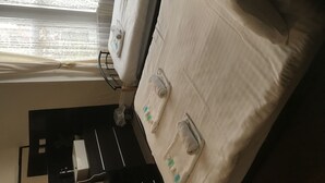 A room with a bed, a window with blinds, and a small table with a lamp. - South Dene Hotel (Bridlington)