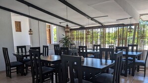 A restaurant with multiple tables and chairs, a ceiling fan, hanging lights, and a view of greenery outside. - Q-Bar & Guest House (Dar es Salaam)
