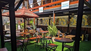An outdoor seating area with wooden tables and chairs, surrounded by greenery and a patterned wall. - Q-Bar & Guest House (Dar es Salaam)