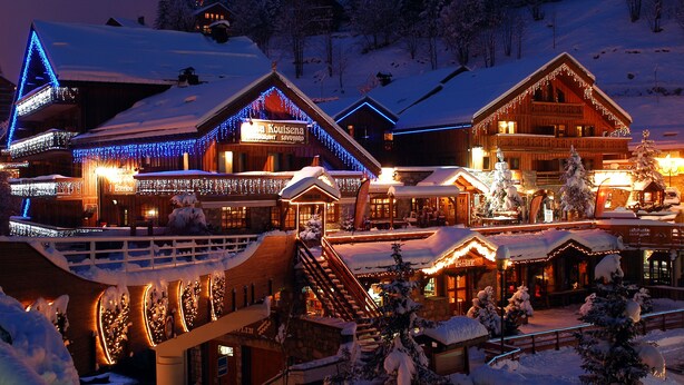 Un edificio cubierto de nieve con letreros iluminados y fachada de madera, rodeado de árboles nevados.