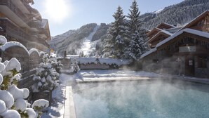 Un complejo turístico en la montaña cubierto de nieve, con un área de piscina despejada, cabañas de madera y vistas del paisaje nevado.