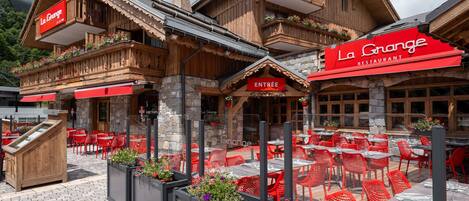 Un restaurante con terraza, paredes de piedra y detalles en rojo.