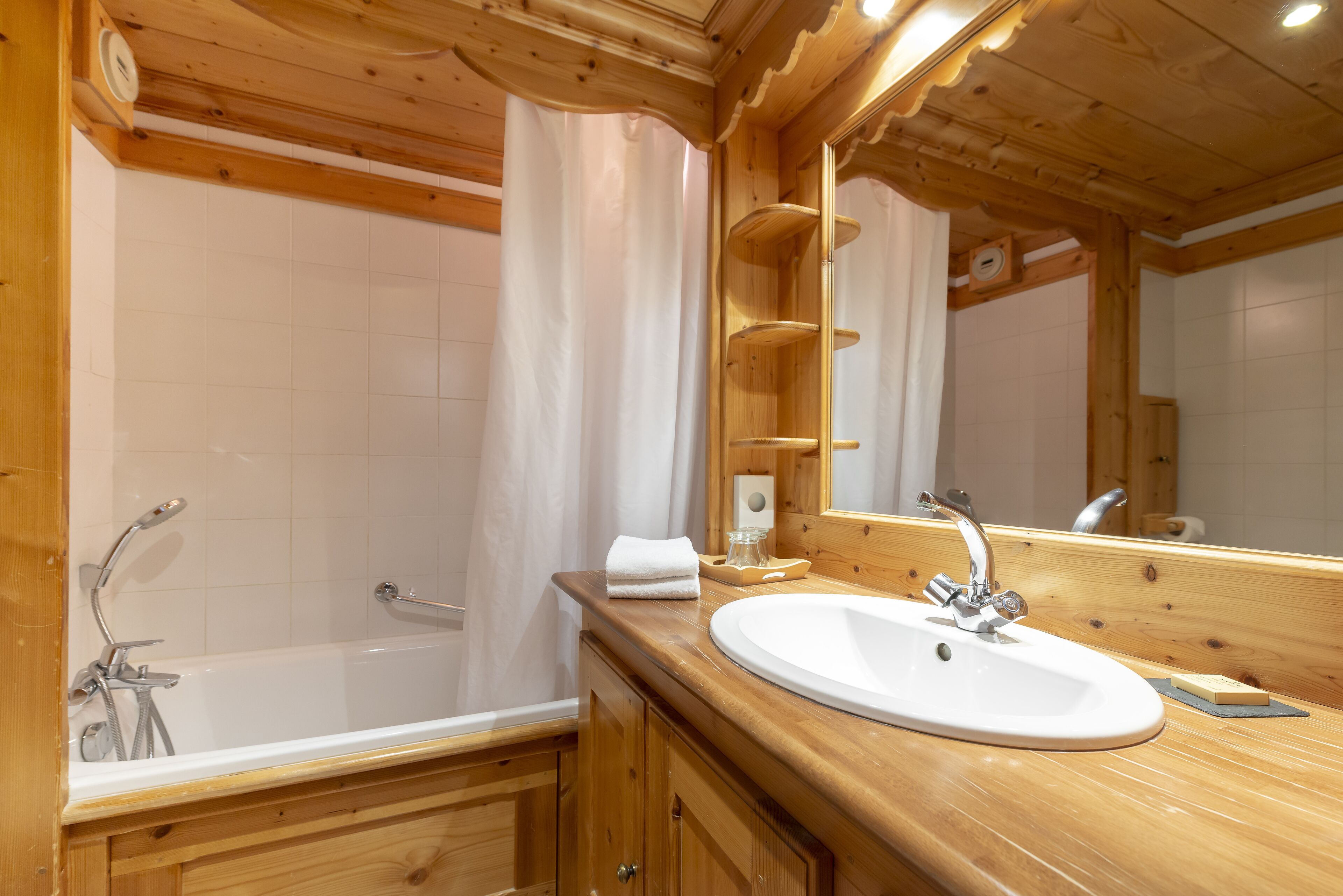 A wooden bathroom with a bathtub, a sink, and a mirror.