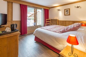 A hotel room with a bed, a TV, a coffee maker, and a window with curtains. - Hôtel L'Eterlou (Les Allues)