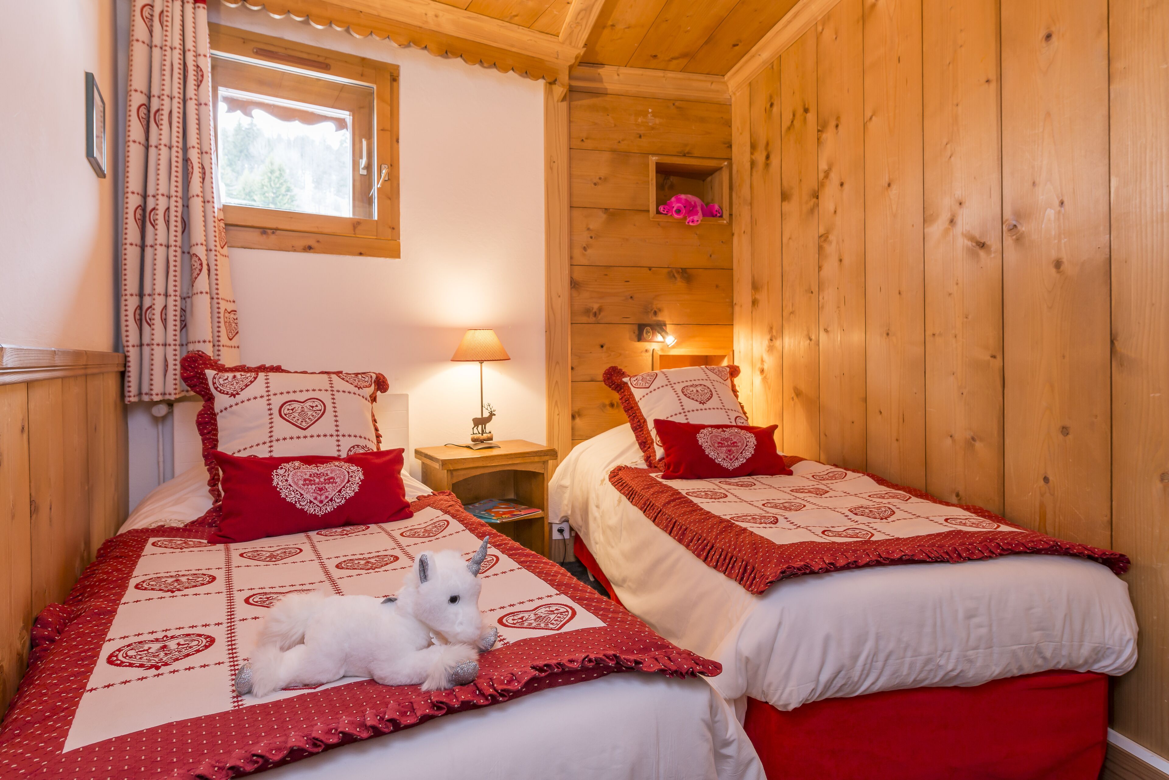 Two wooden-paneled bedrooms with matching red and white bedding, a small window, and a nightstand with a lamp.