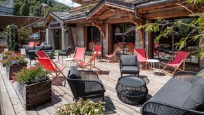 Una cabaña de madera con terraza, mobiliario exterior y macetas con flores.