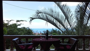 A round table with four chairs on a balcony, overlooking a coastal view with palm trees and houses. - Freedom Estate (Ko Lanta)