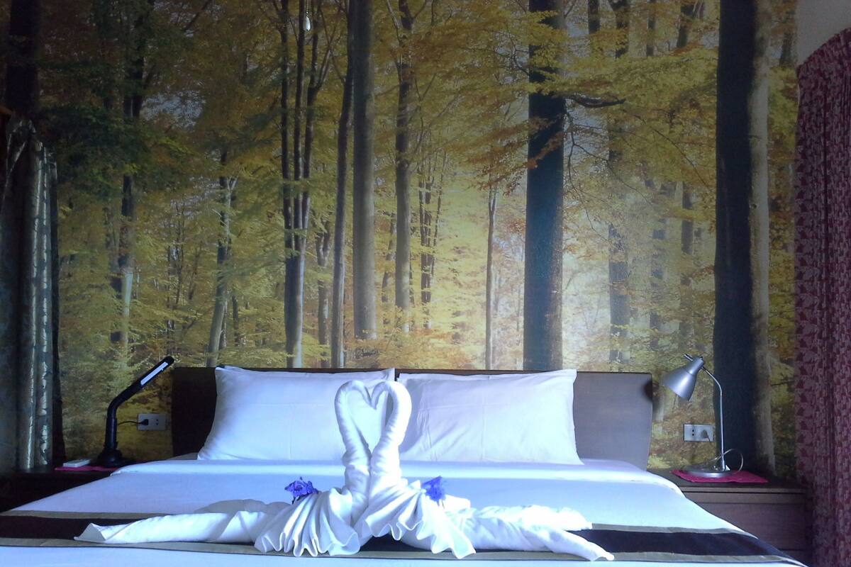 A hotel room with a bed, pillows, a blanket, and a wall mural of a forest.