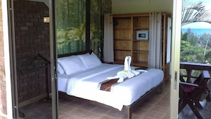 A bedroom with a bed, a wooden wardrobe, a small table, and a view of the outdoors. - Freedom Estate (Ko Lanta)