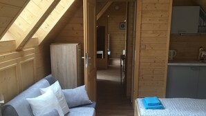 Una habitación acogedora con techo de madera, un sofá con cojines, una cama con colcha estampada y una pequeña cocina.