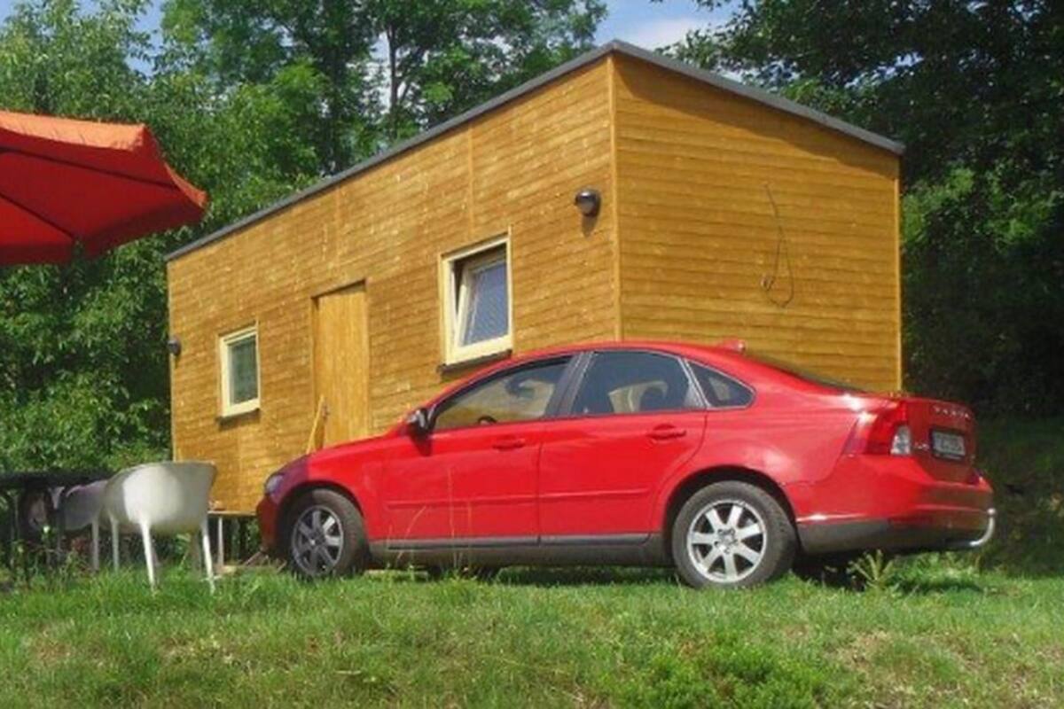 Una cabaña de madera pequeña con un coche rojo estacionado adelante.