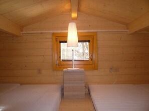 Een blokhut met twee bedden, een raam met lamp en houten wanden.