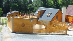 Una cabaña de madera con techo inclinado, terraza cercada y una pequeña zona de estar al aire libre.