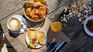Een ontbijtsetting met croissants, koffie, fruit en een glas sap op een houten tafel.