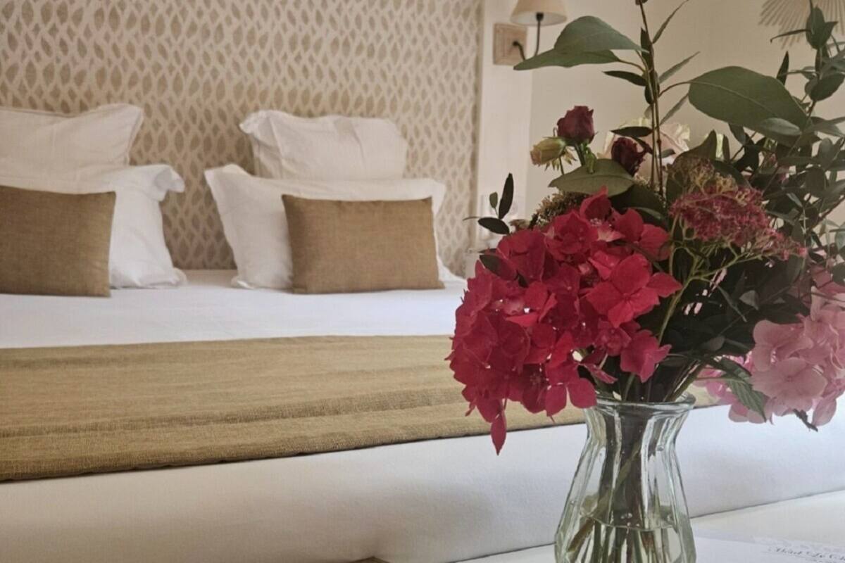 Una habitación de hotel con una cama, un florero y un folleto marrón sobre la mesa.