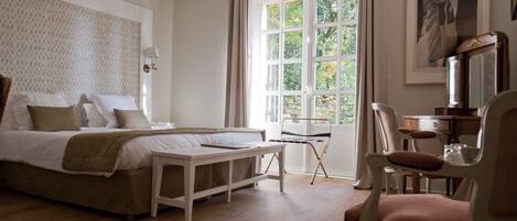 Une chambre à coucher comprenant un lit, une table de chevet, une chaise, un bureau et une fenêtre avec des rideaux.