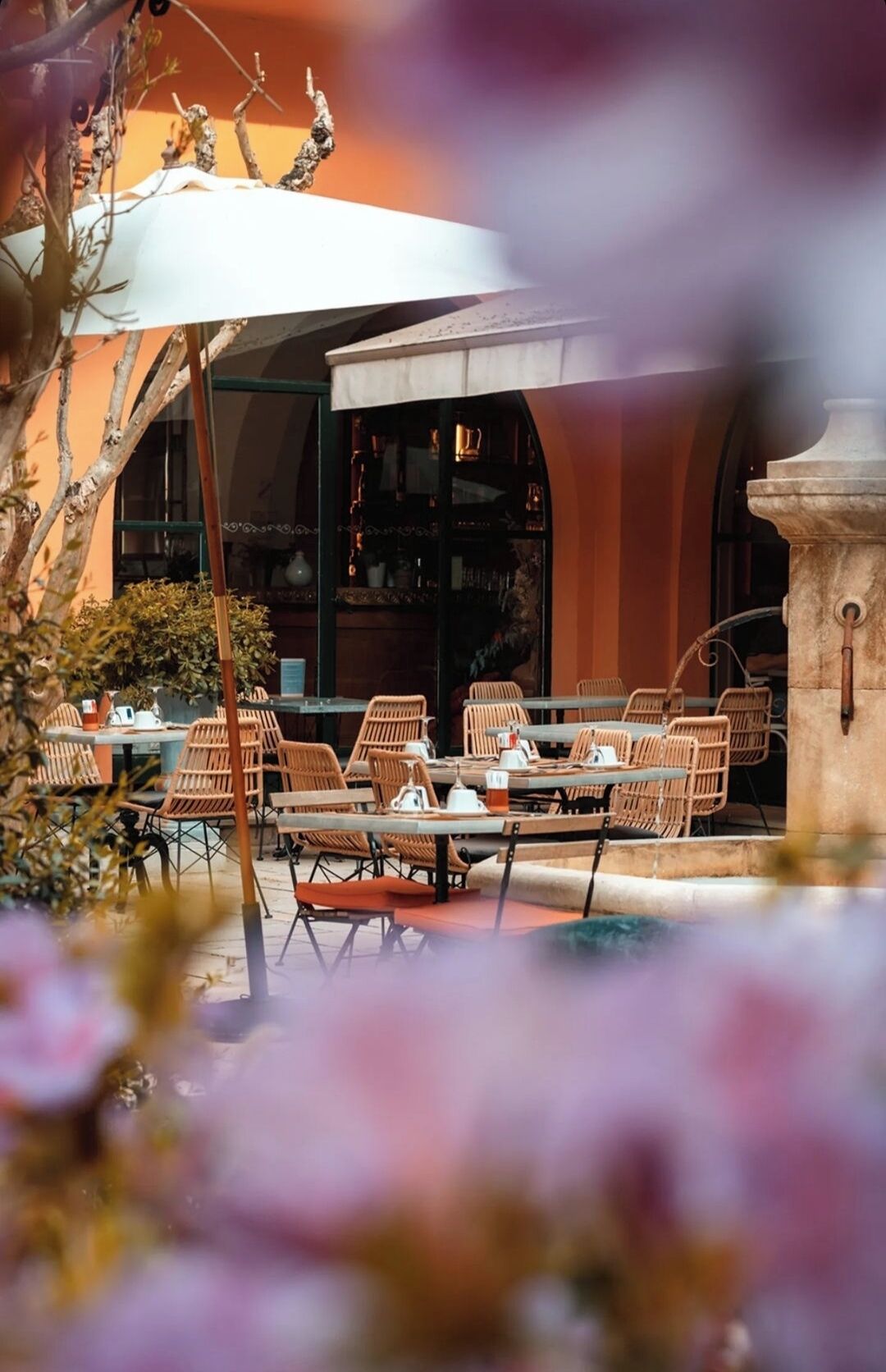 An outdoor seating area with wicker chairs and tables, a white umbrella, and a stone pillar.