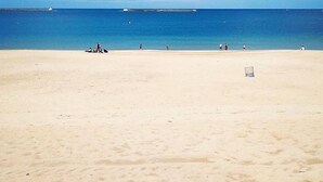Una playa amplia de arena, cielo azul despejado y mar en calma.