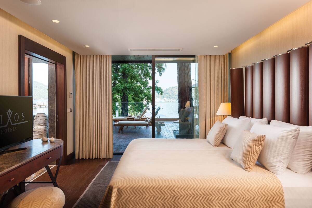 Ein Hotelzimmer mit einem großen Bett, einem Schreibtisch mit Fernseher und Blick auf einen Balkon mit Tisch und Stühlen.