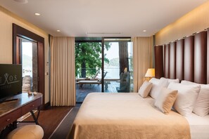 A hotel room with a large bed, a desk with a TV, and a view of a balcony with a table and chairs.
