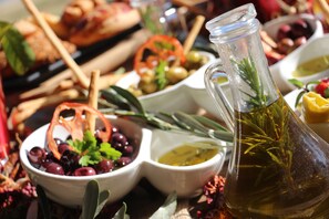 A table with various food items including olives, a bowl of grapes, and a bottle of olive oil.