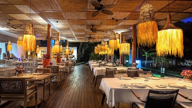 A restaurant with wooden flooring, white tablecloths, and hanging lamps.