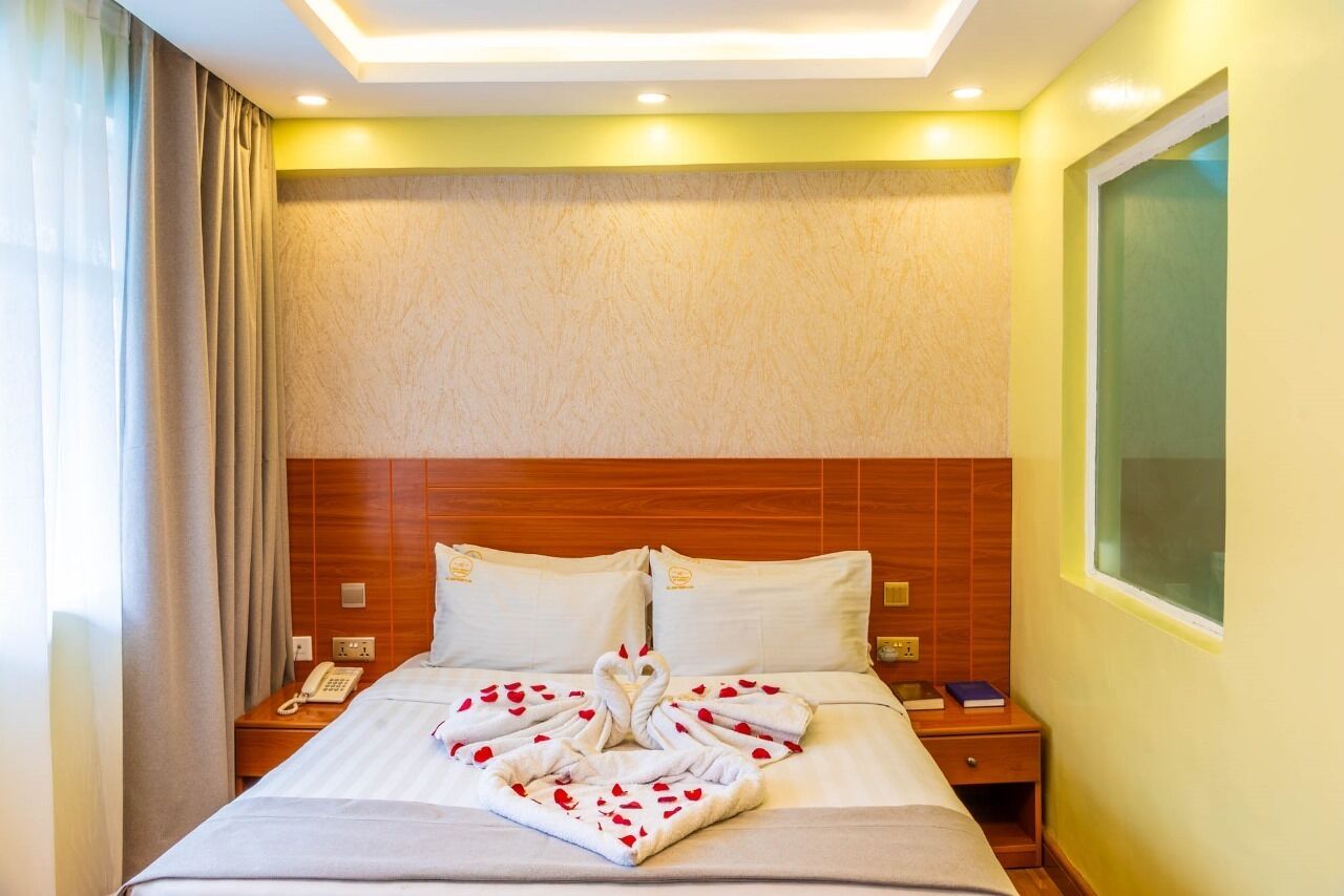 A hotel room with a bed, a wooden headboard, a bedside table with a phone, and a window with curtains.