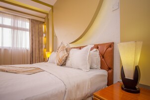 Una habitación de hotel con una cama grande, una mesita de noche de madera, una lámpara y una ventana con cortinas.