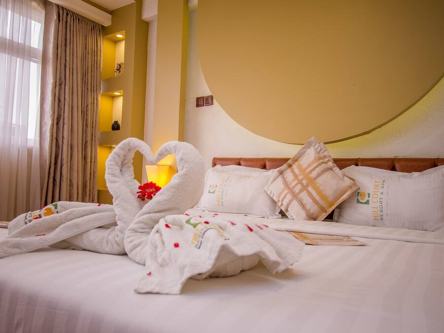 Una habitación de hotel con una cama, una toalla dispuesta en forma de corazón y una almohada con el logotipo del hotel.