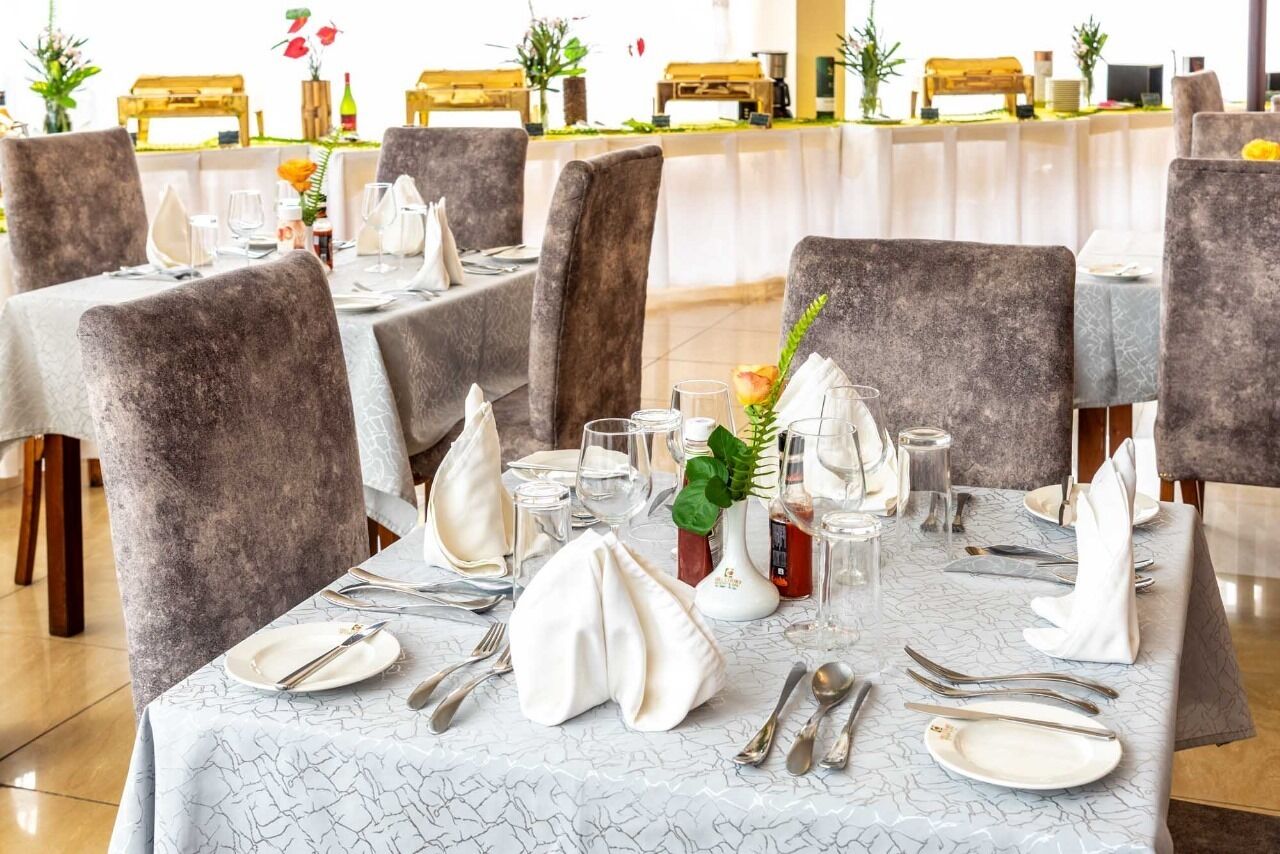 A restaurant with tables set for dining, featuring grey upholstered chairs and white tablecloths.