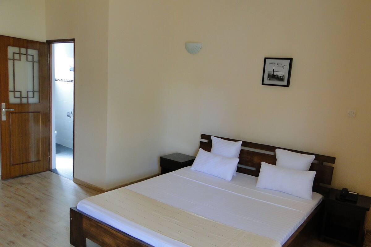 Un dormitorio con cama de madera, ropa de cama blanca, una mesita de noche, una lámpara de pared y un cuadro enmarcado.