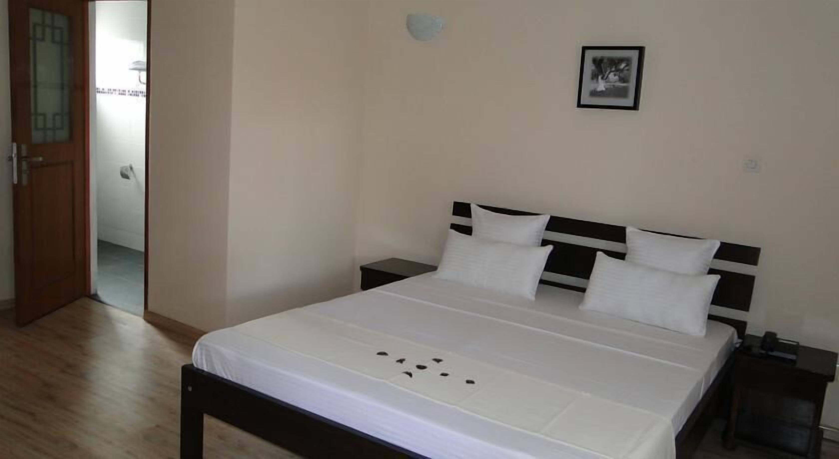 A bedroom with a bed, a nightstand, a door, and a wall-mounted picture.
