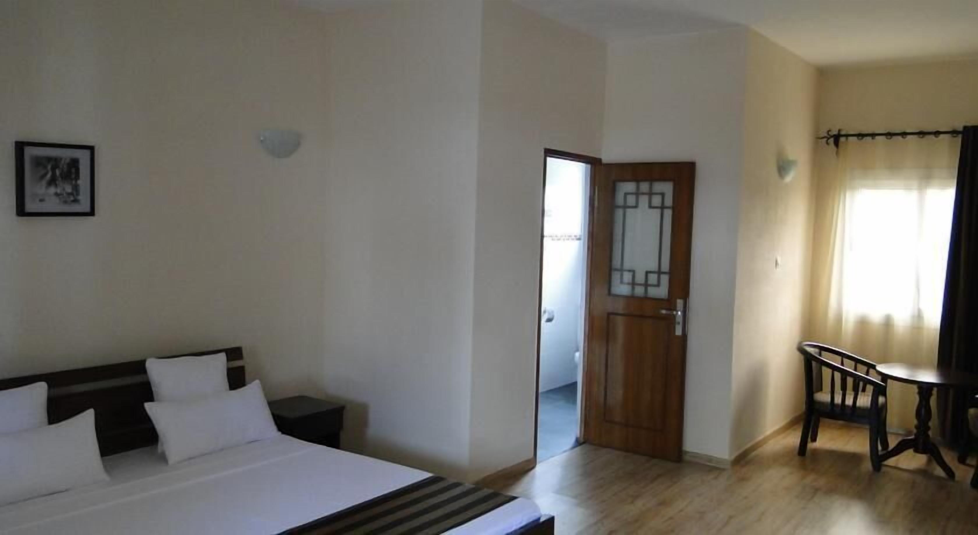 A hotel room with a bed, a small table, and a door leading to another room.