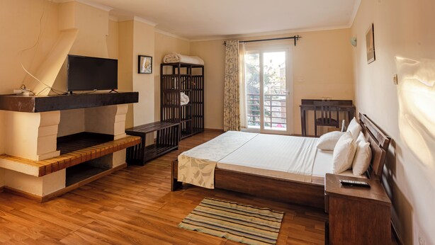 Un dormitorio con cama de madera, televisor en un mueble, una mesita y un balcón con vistas.